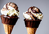 Appetizing sweet ice cream scoops with chocolate topping in waffle cones against gray background