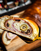 From above of delicious baked ham and olive bread served in bakery against blurred background