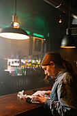 Side view of focused female worker using calculator to count income while sitting at counter with documents during work in cafe