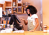 Young African American female seller in apron and glasses touching screen of modern cash register during work in zero waste grocery store