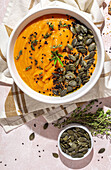 Top view of white ceramic bowl with delicious healthy pumpkin cream soup with seeds and rosemary placed on table in kitchen