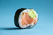Closeup of tasty Japanese Futomaki Norwegian sushi roll with fresh salmon and avocado served against blue background in light studio