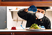 Serious male chef working in kitchen of restaurant and adding salt on dish in plate