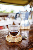 Glass of hot fresh drink from moka pot on wooden counter in coffee house