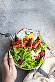 Healthy lunch with fresh organic vegetable salad, fried egg and sausages served on the concrete table
