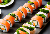 Köstliche frische Sushi-Rollen mit Lachs und Avocado und Reis serviert mit Salatblättern auf einem schwarzen Brett