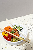 From above bamboo chopsticks placed on top of bowl with tasty poke dish on table covered with sesame seeds