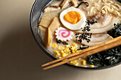 Appetitanregende japanische Ramen mit gekochtem Ei und Pilzen, serviert in einer Schüssel mit Holzstäbchen vor beigem Hintergrund