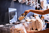 Unrecognizable female using metal scoop to take portion of granola from glass box while visiting eco friendly grocery store