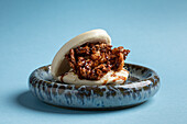 Delicious Japanese pan bao bun with fried soft shell crab served on ceramic plate against blue background in light studio