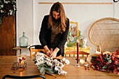 Calm female florist standing at table and arranging bouquet of flowers in creative floristry studio