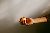 Crop anonymous person holding ripe apple on gray background