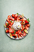 Top view of appetizing fresh strawberries and lemon served with burrata cheese on plate