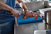 Side view of young male cook in casual clothes and apron cutting sweet potato while working in restaurant kitchen