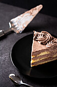 Von oben auf ein Stück leckeren Trüffel-Schokoladenkuchen, der in einem Teller auf einem schwarzen Tisch mit Löffel und Spachtel serviert wird