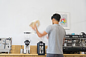 Back view of anonymous male barista pouring coffee beans from bag into modern professional coffee grinder at wooden counter in coffee house