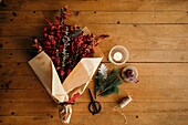 From above of Christmas bouquet in wrapping paper placed near scissors and decorative equipment on wooden table in daylight