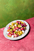 Frische reife Trauben, Oliven, Feigen und Mozzarella auf einem Teller auf grünem und rosa Tischhintergrund