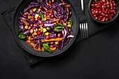 Homemade Purple Cabbage Salad with Corn, Carrots, Pomegranate and Spinach on dark background. Vegan food concept. Healthy food