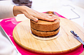 Crop unrecognizable person pressing hand to top of cake on wooden stand in bakery