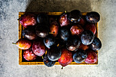 Fresh organic and ripe plum fruits in wooden box on concrete background