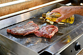 High angle of crop anonymous male chef pouring oil on raw meat pieces while cooking on stove