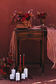 Wooden old fashioned table decorated with fabric and vases of red flowers near burning candles in studio