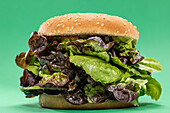 Fresh burger bun with bunch of fresh mesclun leaves as concept of healthy food against green background