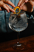 Soft focus of cropped unrecognizable female barkeeper putting with tongs lemon zest into glass with ice cubes while making cocktail in bar