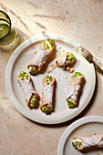 Top view of delicious Italian cannoli dessert with cream cheese and pistachio nuts placed on white plate with fork