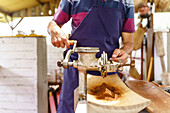 Unbekannter männlicher Angestellter in Schürze mahlt Kaffeekörner mit einem manuellen Metallwolf in ein Brett in einem Landhaus