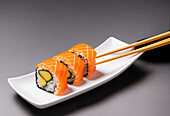 Appetizing sushi rolls with rice and avocado wrapped in raw salmon served on plate with soy