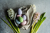 Von oben Frühlingsgedeck mit Hyazinthenblüten und bunten Eiern auf grauem Betontisch für festliches Abendessen