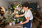 Side view of crop anonymous female florist standing with green plant in glass terrarium in floral shop