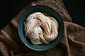 Top view of uncooked noodles for ramen preparation placed in bowl on brown tablecloth