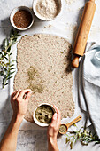 Top view of anonymous person adding spices into raw dough while cooking pastry in kitchen near rolling pin and ingredients