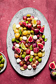 From above fresh ripe grapes, olives, figs and mozzarella seasonal christmas salad placed on plate on red tabletop background