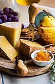 Different kinds of cheese, fruits and jams on wooden cutting board ready for party