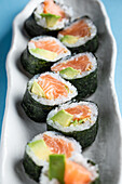 From above set of tasty Futomaki Norwegian sushi rolls with salmon and avocado served on blue background in light studio