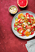 Top view of healthy salad with oranges and strawberries and apples and cucumbers served with cheese and pistachios on plate