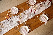 From above of white tablecloth and plates placed on festive table decorated with burning candles and dry branches of tree