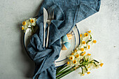 From above spring table setting with ceramic plate near daffodil flowers on concrete background