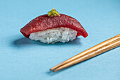 Traditionelle japanische köstliche Blauflossen-Nigiri mit Reis und frischem Thunfisch mit scharfem Wasabi, serviert mit Stäbchen auf blauem Hintergrund in einem hellen Studio