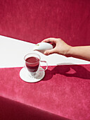 From above hand of crop anonymous person pouring cream into tasty Irish coffee placed on red background in light studio