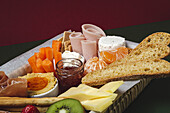 Brunch box with assorted sliced meats various types of cheese and crispbreads arranged near ripe cup kiwi sweet strawberries and peeled mandarin near jam in glass jar on colorful background