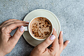 Top view of the ceramic cup of cappuccino with foam in the woman's hands