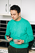 Adult male with cup of aromatic coffee text messaging on cellphone in light house