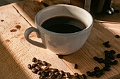 Fresh coffee in white ceramic cup near pile of freshly roasted coffee beans served on wooden table near French press