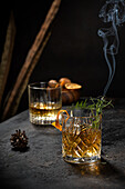 Crystal glass of old fashioned whiskey drink garnished with fresh rosemary and orange peel on black table