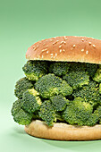 Halves of burger bun with bunch of raw broccoli served on green background during healthy lunch